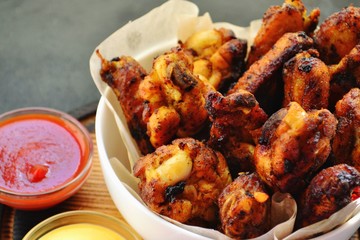 Fried chicken wings. Chicken wings on a dark background. Barbecue meat, grill. Sauce in bowls, ketchup, mayonnaise, mustard, cheese sauce. Appetizing fried meat in the white plate. bowl.