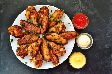 Fried chicken wings. Chicken wings on a dark background. Barbecue meat, grill. Sauce in bowls, ketchup, mayonnaise, mustard, cheese sauce. Appetizing fried meat in the white plate. bowl.