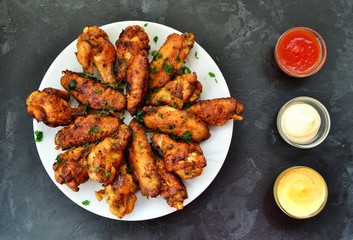 Fried chicken wings. Chicken wings on a dark background. Barbecue meat, grill. Sauce in bowls, ketchup, mayonnaise, mustard, cheese sauce. Appetizing fried meat in the white plate. bowl.