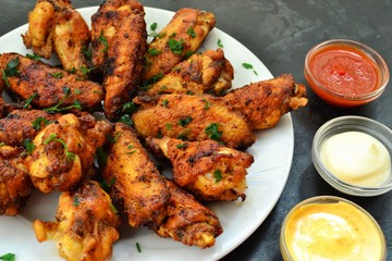 Fried chicken wings. Chicken wings on a dark background. Barbecue meat, grill. Sauce in bowls, ketchup, mayonnaise, mustard, cheese sauce. Appetizing fried meat in the white plate. bowl.