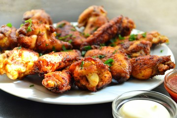 Fried chicken wings. Chicken wings on a dark background. Barbecue meat, grill. Sauce in bowls, ketchup, mayonnaise, mustard, cheese sauce. Appetizing fried meat in the white plate. bowl.