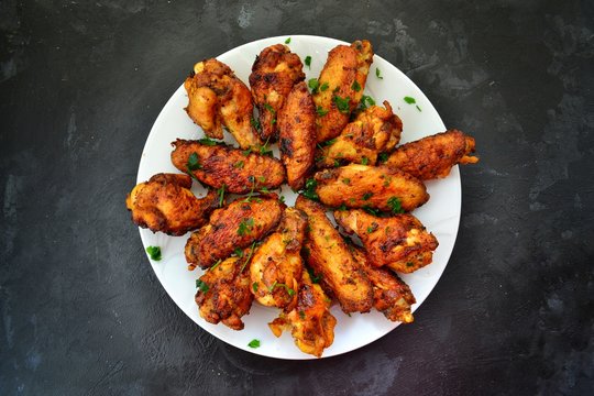 Fried chicken wings. Chicken wings on a dark background. Barbecue meat, grill. Sauce in bowls, ketchup, mayonnaise, mustard, cheese sauce. Appetizing fried meat in the white plate. bowl.