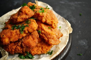 Appetizing food on a black dark table background. Chicken nuggets on parchment. Nuggets on a wooden board. Fried chicken fillet.