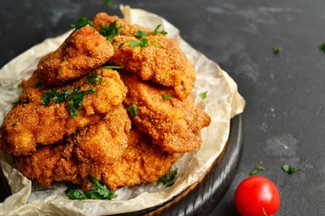 Appetizing food on a black dark table background. Chicken nuggets on parchment. Nuggets on a wooden board. Fried chicken fillet.