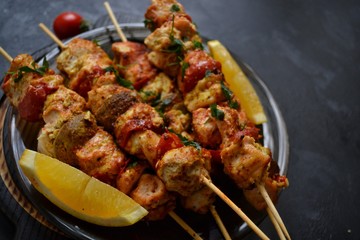 Appetizing food on a dark background. Chicken skewers with mushrooms and tomato. Oven skewered chicken fillet. Chicken kebab on the wooden board and black plate.
