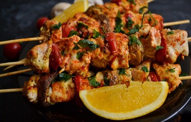 Appetizing food on a dark background. Chicken skewers with mushrooms and tomato. Oven skewered chicken fillet. Chicken kebab on the wooden board and black plate.