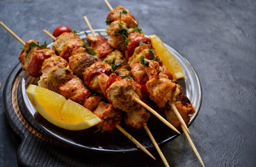 Appetizing food on a dark background. Chicken skewers with mushrooms and tomato. Oven skewered chicken fillet. Chicken kebab on the wooden board and black plate.