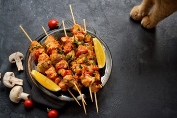 Appetizing food on a dark background. Chicken skewers with mushrooms and tomato. Oven skewered chicken fillet. Chicken kebab on the wooden board and black plate.