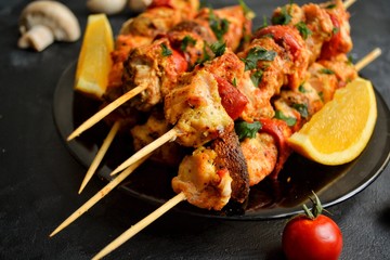 Appetizing food on a dark background. Chicken skewers with mushrooms and tomato. Oven skewered chicken fillet. Chicken kebab on the wooden board and black plate.