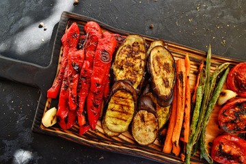 Grilled vegetables on a wooden board. Appetizing grilled vegetables in on a dark background,...