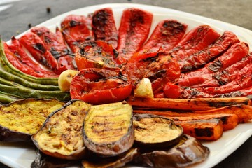 Grilled vegetables on a white plate. Appetizing grilled vegetables in a plate on a dark background, close-up. Vegetarian wholesome food. Baked eggplant, bell peppers, tomatoes, asparagus and carrots.