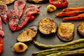 Grilled vegetables on a wooden board. Appetizing grilled vegetables in on a dark background, close-up. Vegetarian wholesome food. Baked eggplant, bell peppers, tomatoes, asparagus and carrots.