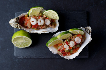 Oyster shell with seafood salad and lime on dark background