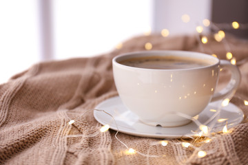 Cup of coffee with glowing garland on plaid