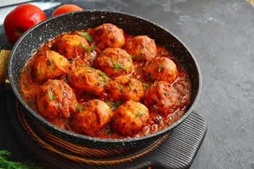 Meatballs in tomato sauce. Chicken meatballs. Meatballs in a pan on a dark table background isolated.