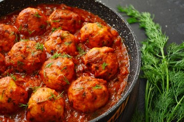 Meatballs in tomato sauce. Chicken meatballs. Meatballs in a pan on a dark table background isolated.