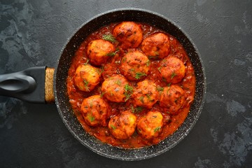 Meatballs in tomato sauce. Chicken meatballs. Meatballs in a pan on a dark table background isolated.