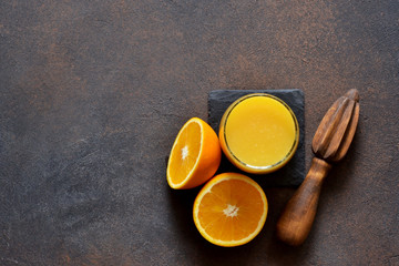 Orange juice, oranges and and juicer on stone background. Top view with copy space