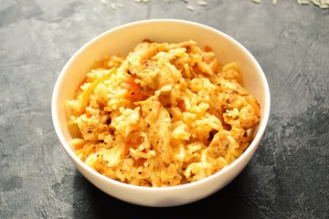 Rice in a white bowl. Rice dish on a dark table background. Pilaf, rice porridge, cooked rice with vegetables. Healthy vegetarian food.