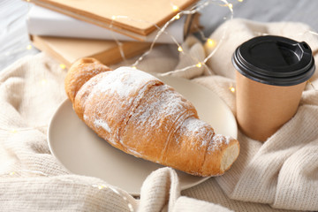 Plate with croissant, sweater, cup of coffee and garland on table