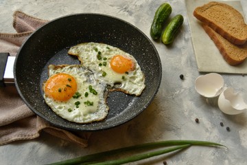 Tasty breakfast. Food on the table. Food on a light gray decorative background. Fried eggs in a pan. Eggs, green onions, brown bread, cucumbers.