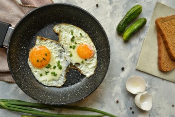 Tasty breakfast. Food on the table. Food on a light gray decorative background. Fried eggs in a pan. Eggs, green onions, brown bread, cucumbers.