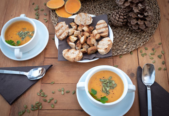 Meal ready for two people. White bowls with pumpkin cream soup. In the middle of the rustic wooden table bread croutons.