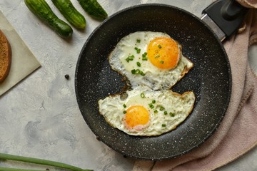 Tasty breakfast. Food on the table. Food on a light gray decorative background. Fried eggs in a pan. Eggs, green onions, brown bread, cucumbers.