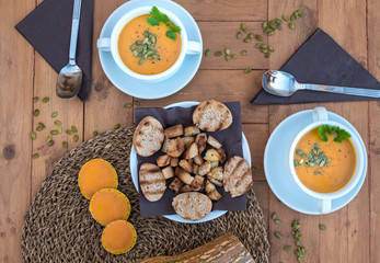Meal ready for two people. White bowls with pumpkin cream soup. In the middle of the rustic wooden table bread croutons.