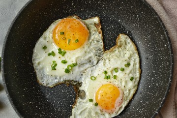 Tasty breakfast. Food on the table. Food on a light gray decorative background. Fried eggs in a pan. Eggs, green onions, brown bread, cucumbers.