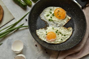 Tasty breakfast. Food on the table. Food on a light gray decorative background. Fried eggs in a pan. Eggs, green onions, brown bread, cucumbers.