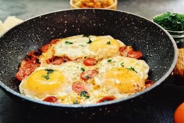 Fried eggs with tomatoes and parsley. Fried eggs in a black pan on a dark background. Scrambled Egg Ingredients