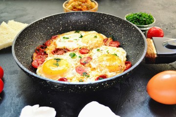 Fried eggs with tomatoes and parsley. Fried eggs in a black pan on a dark background. Scrambled Egg Ingredients