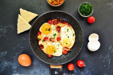 Fried eggs with tomatoes and parsley. Fried eggs in a black pan on a dark background. Scrambled Egg Ingredients