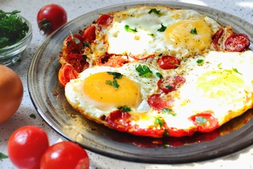 Fried eggs with tomatoes and parsley. Fried eggs in a black plate on a dark background.