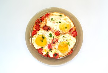 Fried eggs with tomatoes and parsley. Fried eggs in a plate on the white background isolated.