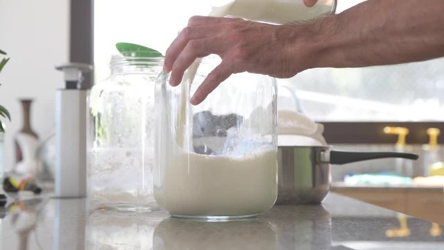 A man in the kitchen adds fresh milk in a new kefir preparation, stirs and stores for 24 hours to have a health probiotic aliment daily. A superfood