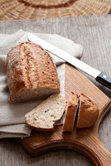 Loaf of whole wheat bread with slices on wooden board on kitchen table