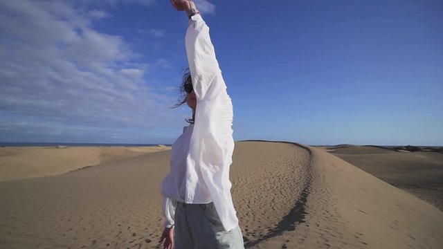 Beautiful young woman waving and stretching in the windy dunes in the desert. Gran Canaria, Spain
