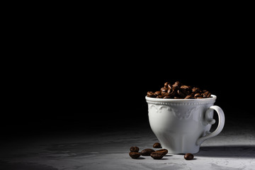 Porcelain coffee cup on a concrete table. Concrete surface. Marble surface. Black background. Coffee beans. Fried arabica. Coffee mug. White porcelain. Clear shadows.