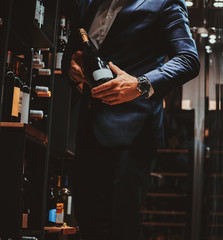 Elegant man in suit at wine cellar with bottle of wine