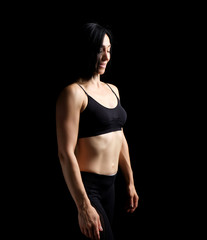 Fototapeta na wymiar Adult girl with a sports figure in black bra and black shorts standing on a dark background