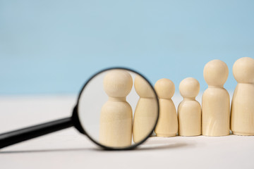 Wooden figures of people under magnifying glass on blue background.