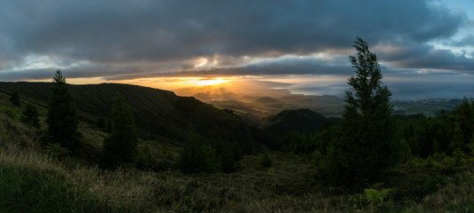 Stunning sunset panorama of the volcanic landscape on the island of São Miguel in the Azores archipelago. Volcanic cones are illuminated by sun rays under a dramatic cloudy sky with the Atlantic Ocean
