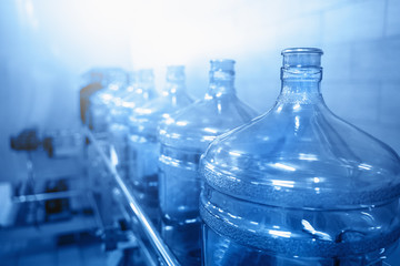 Water bottling conveyor line with plastic bottles or gallons on water factory production, blue toned with selective focus