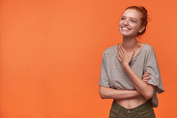 Attractive young readhead female showing her pleasant emotions over orange background, wearing her...