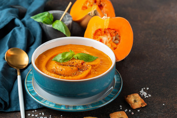 Pumpkin soup in a blue bowl served with basil. Vegan soup.  Braun stone background. 