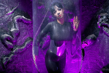 Shot of a futuristic young person posing behind glass space capsule with wires and purple neon light on black background