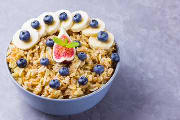 Healthy breakfast. Oatmeal with blueberries, banana and figs. Oatmeal with fruits and berries in a bowl. Cooked oatmeal on cement background. Copy space