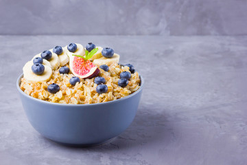 Healthy breakfast. Oatmeal with blueberries, banana and figs. Oatmeal with fruits and berries in a bowl. Cooked oatmeal on cement background. Copy space